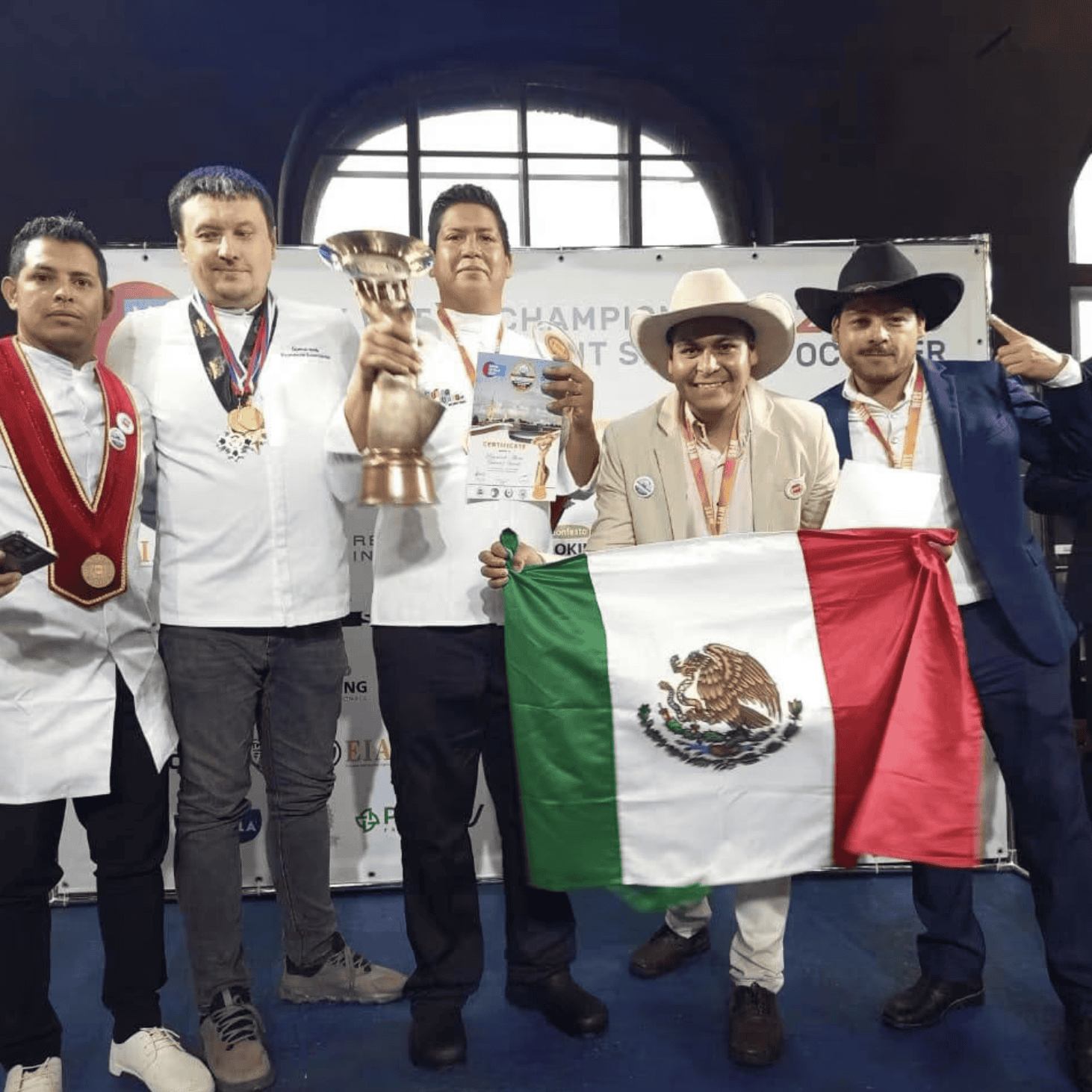Equipo mexicano con trofeo y bandera de México en podium.