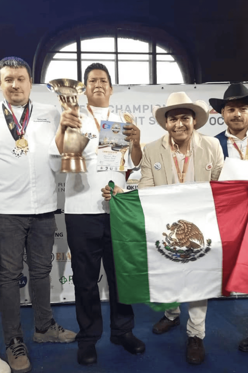 Equipo mexicano con trofeo y bandera de México en podium.