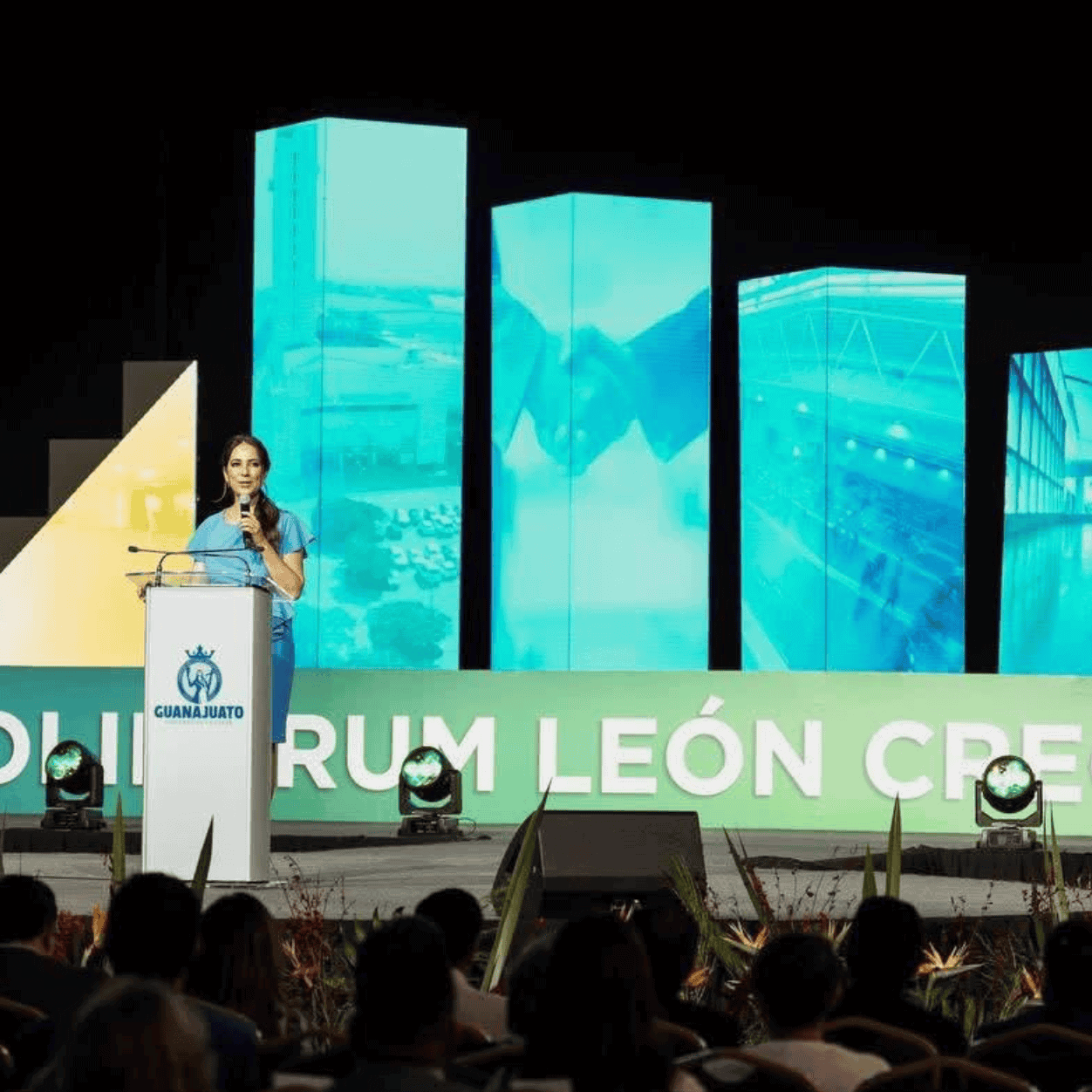 Discurso en evento de reconocimiento en el Poliforum León, con pantallas digitales de fondo.