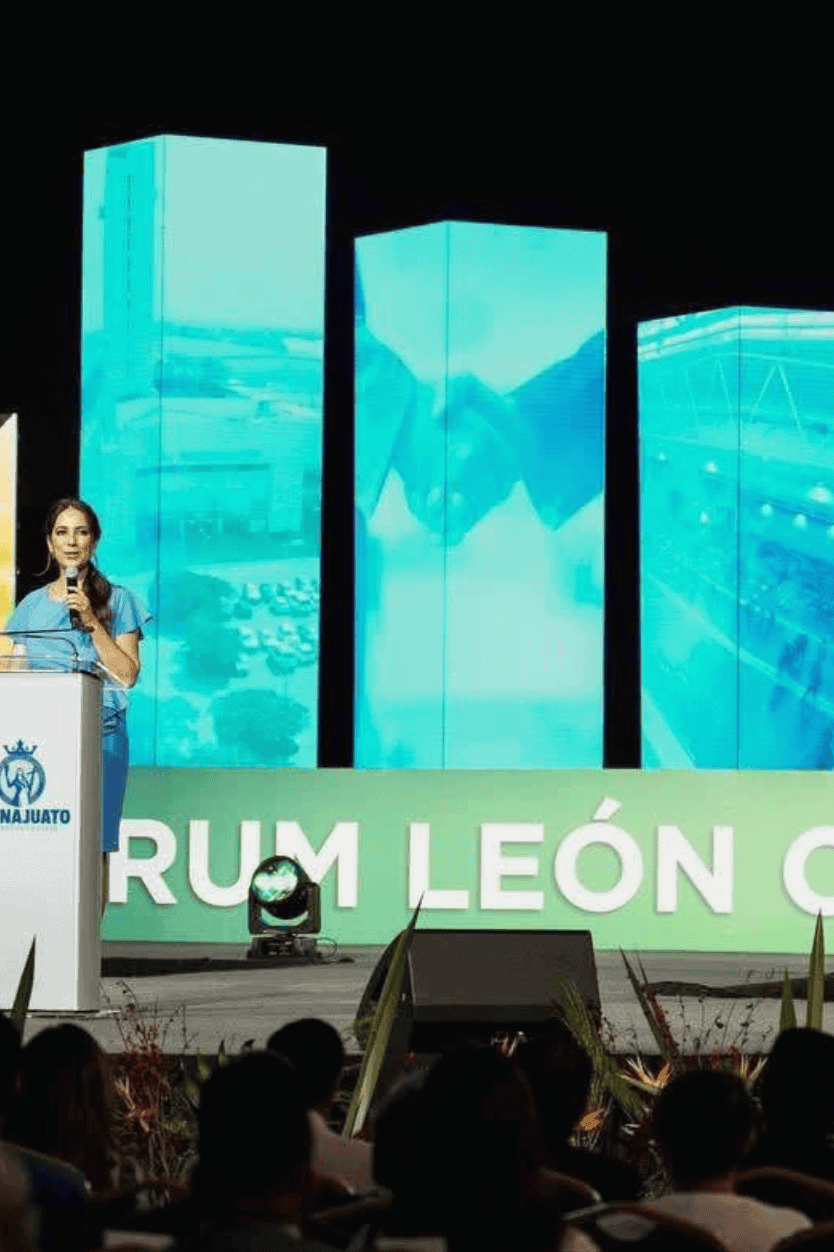 Discurso en evento de reconocimiento en el Poliforum León, con pantallas digitales de fondo.