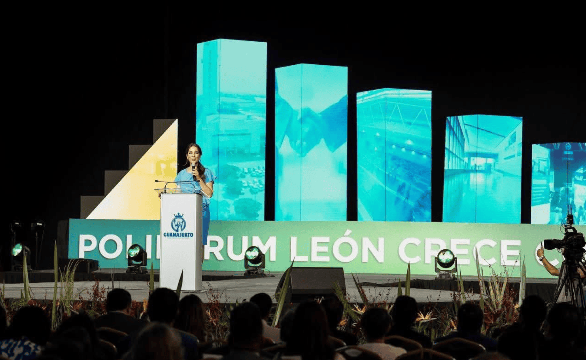 Discurso en evento de reconocimiento en el Poliforum León, con pantallas digitales de fondo.