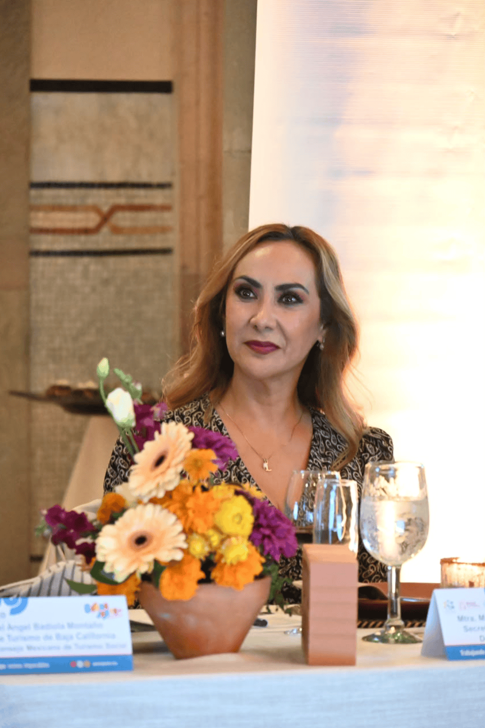 Mujer en evento de turismo en Guanajuato con flores y bebidas en la mesa.