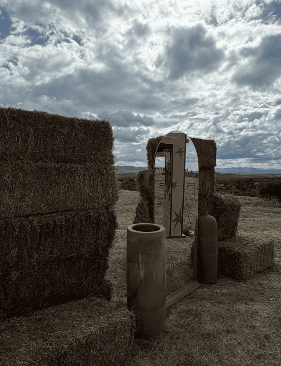 Espejo decorativo en campo de heno con cerámicas y cielo nublado.